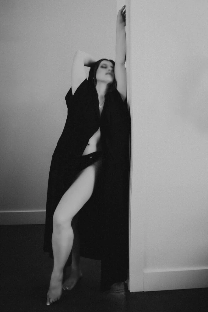 A monochrome portrait of Ava Marie in a flowing dress, dramatically and elegantly positioned against a wall. She showcases an air of contemplation and allure. Ava Marie Halifax's Elite Independent Companion